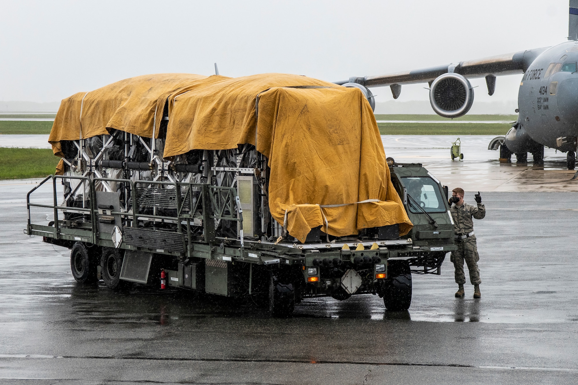 A 436th Aerial Port Squadron Airman guides a K-loader at Dover Air Force Base, Delaware, April 30, 2020. Tarps were placed on top of Transport Isolation Systems due to inclement weather at Dover AFB. In accordance with health protection policies, Dover AFB will serve as the sole hub for TIS decontamination on the East Coast. (U.S. Air Force photo by Senior Airman Christopher Quail)