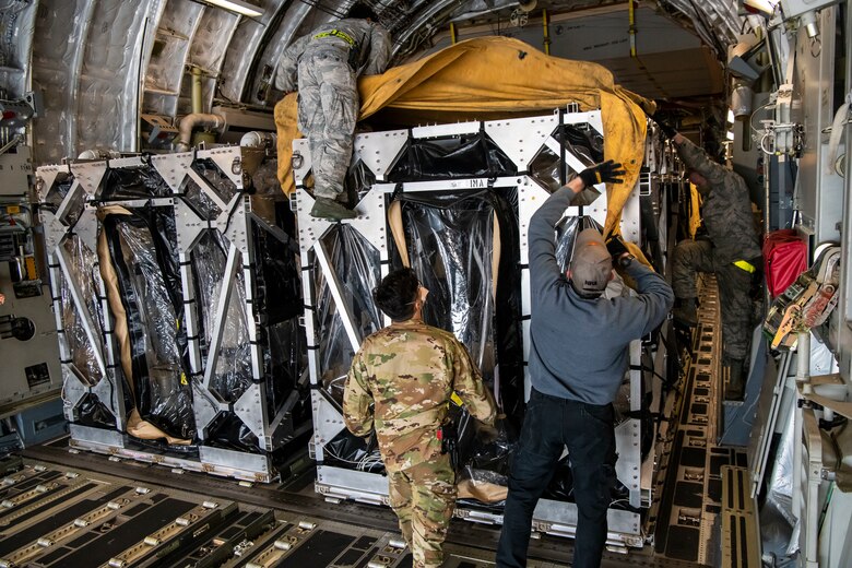 Airmen cover two Transport Isolation Systems with tarps due to inclement weather at Dover Air Force Base, Delaware, April 30, 2020. The TIS units were delivered to Dover AFB by C-17 Globemaster III from Joint Base Charleston, South Carolina. In accordance with health protection policies, Dover AFB will serve as the sole hub for TIS decontamination on the East Coast. (U.S. Air Force photo by Senior Airman Christopher Quail)