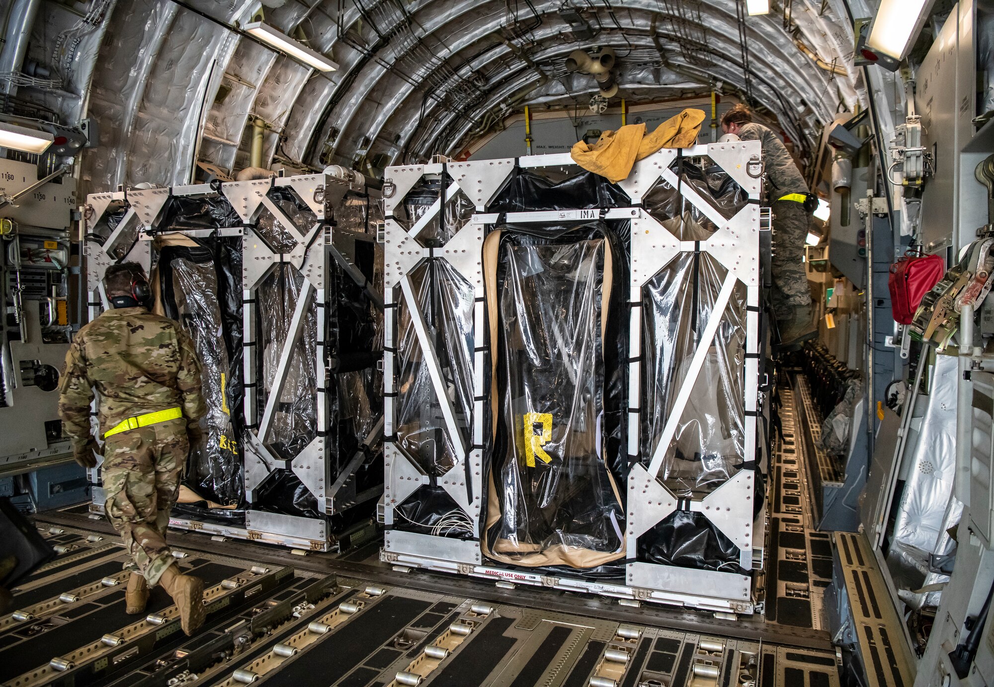 Airmen cover two Transport Isolation Systems with tarps due to inclement weather at Dover Air Force Base, Delaware, April 30, 2020. The TIS units were delivered to Dover AFB by C-17 Globemaster III from Joint Base Charleston, South Carolina. In accordance with health protection policies, Dover AFB will serve as the sole hub for TIS decontamination on the East Coast. (U.S. Air Force photo by Senior Airman Christopher Quail)