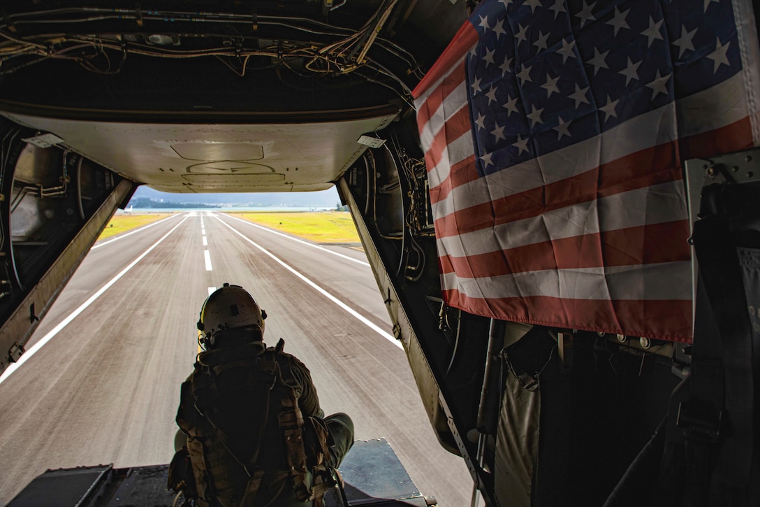A Marine sits inside an aircraft with an American flag displayed on the aircraft’s interior.