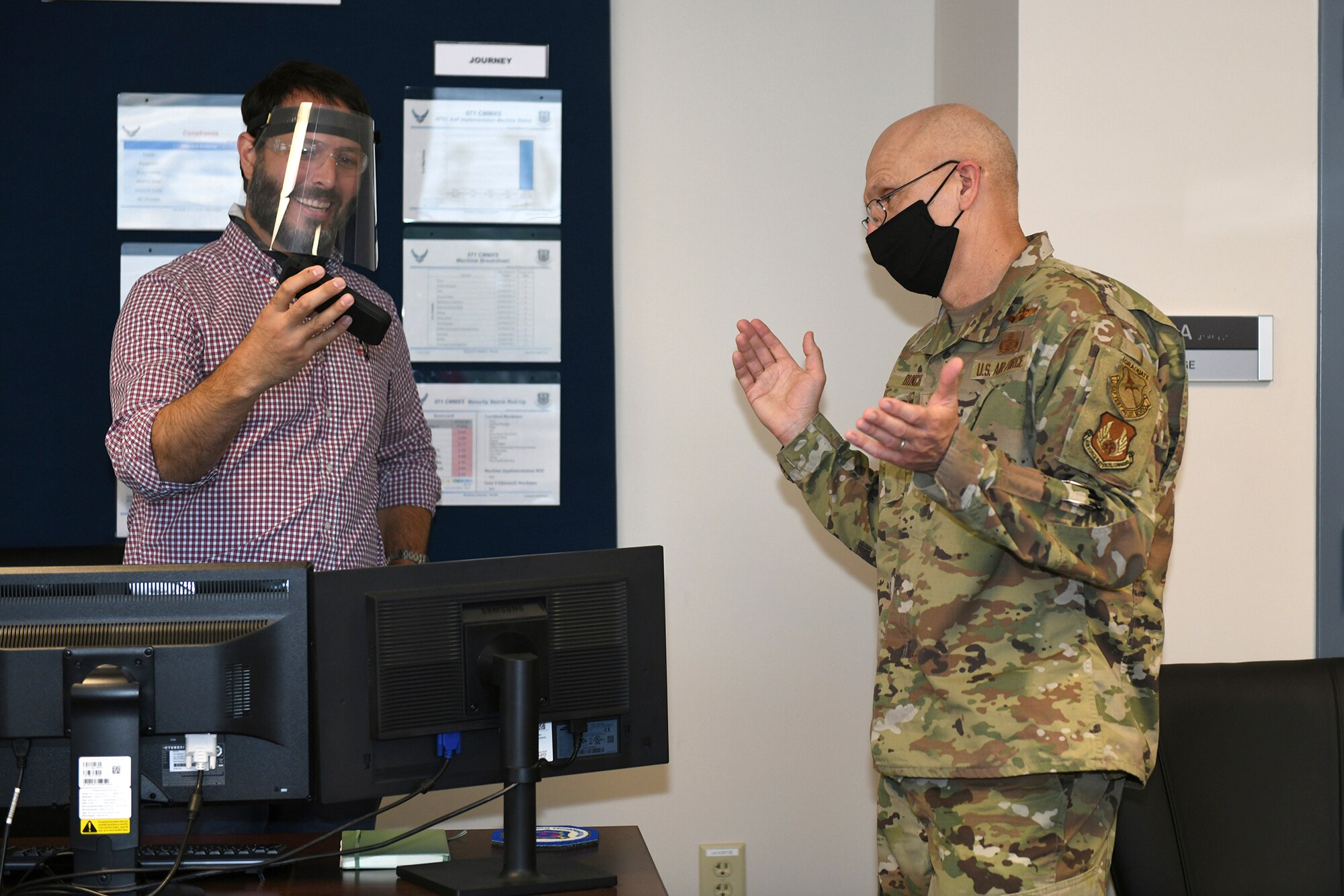 Photos shows the general clapping his hands while Campbell talks on his speaker phone.