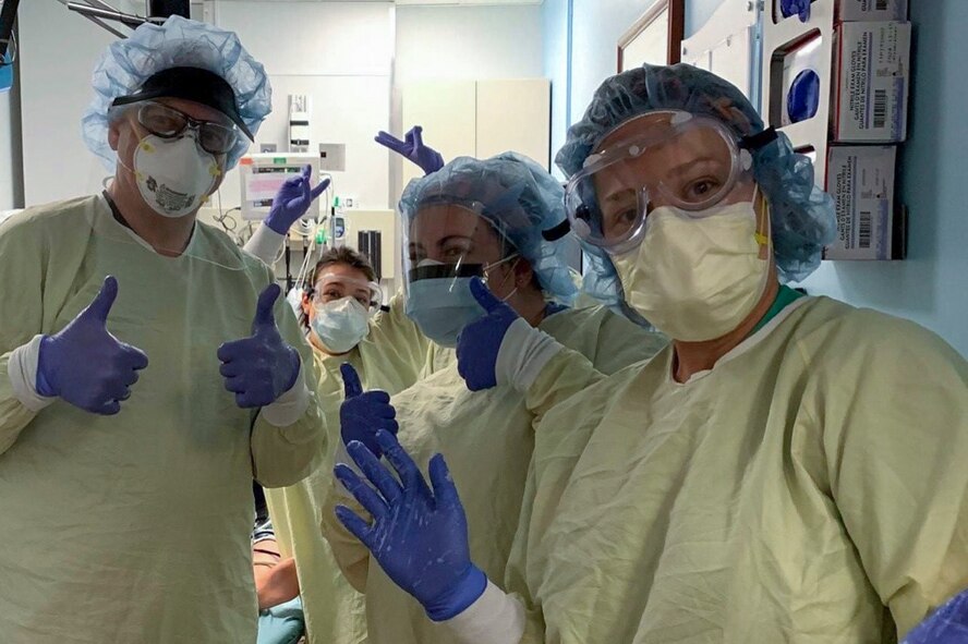 Four medical workers wearing personal protective equipment wave.
