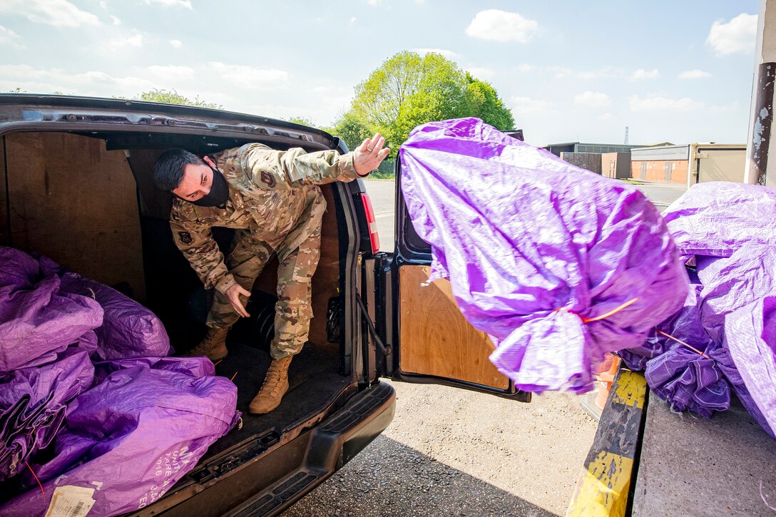 An airman tosses a large purple sack out of the back of a vehicle and onto a loading dock.