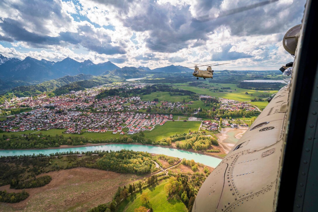 Two Army aircraft fly near each other over a town.