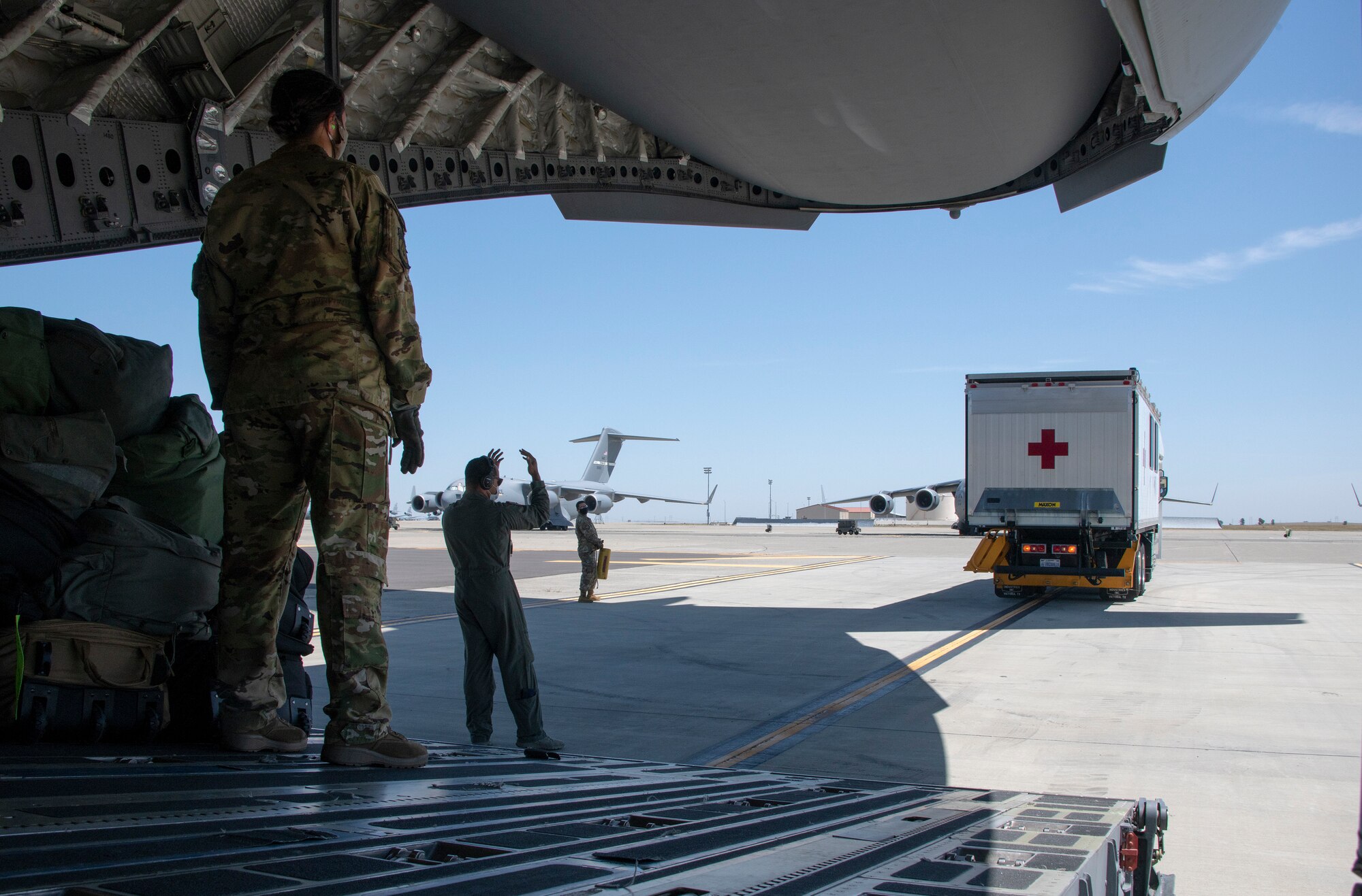 U.S. Air Force Master Sgt. Jesse Williams, 21st Airlift Squadron flight chief of standardization and evaluation, guides a medical recovery vehicle to the cargo door of a C-17 Globemaster III May 7, 2020, at Travis Air Force Base, California. Aeromedical evacuation and aircrew team members took part in a training event focused on the reception and care of a simulated COVID-19 patient utilizing the Transport Isolation System capsule. Travis AFB maintains a TIS loaded C-17 on alert status with to ensure the aircraft is ready to launch at a moment’s notice. The TIS unit allows the transport of individuals with highly contagious diseases without infecting other passengers or aircrew on the aircraft. (U.S. Air Force photo by Heide Couch
