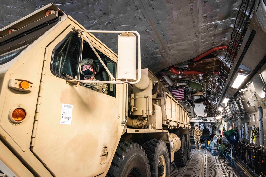 A soldier drives a vehicle onto an aircraft.