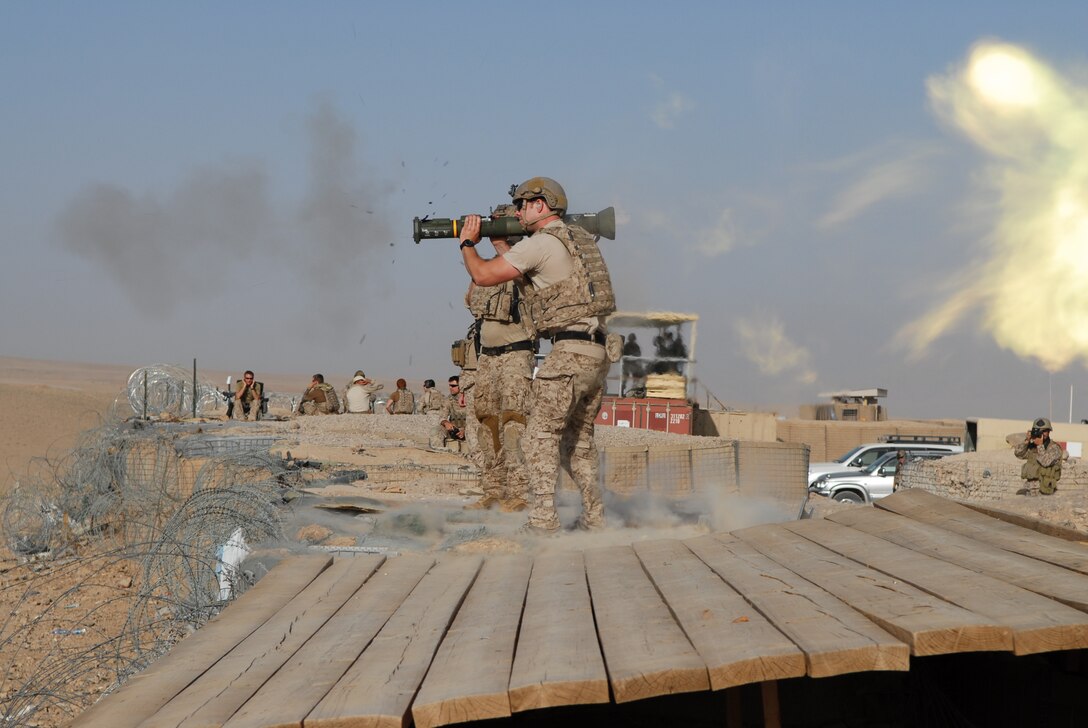 A service member fires a shoulder-launched missile as other service members sit nearby.