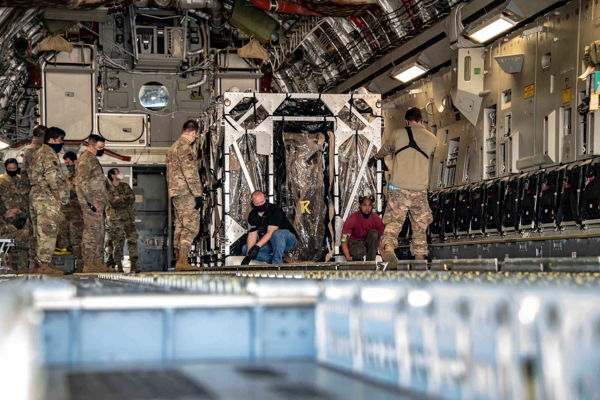 Personnel from the 60th Aerial Port Squadron and medical personnel from the COVID West Aeromedical Evacuation Task Force secure a Transport Isolation System capsule in the cargo bay of a C-17 Globemaster III May 9, 2020, at Travis Air Force Base, California. Travis AFB has a C-17 loaded with a TIS capsule on alert status to ensure the aircraft is ready to launch at a moment’s notice. The TIS unit allows the transport of individuals with highly contagious diseases without infecting other passengers or aircrew on the aircraft. (U.S. Air Force photo by Heide Couch)