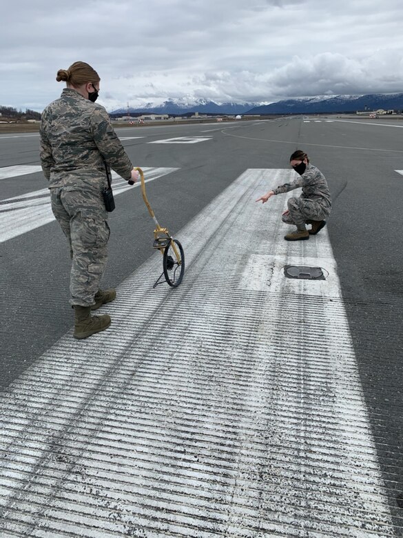 U.S. Air Force Airmen 1st Class Hannah Klein and Leandra Ventura-Perez, 3rd Operations Support Squadron Airfield Management shift lead and operations coordinator, assess airfield pavement damage while wearing protective facemasks at Joint Base Elmendorf-Richardson, Alaska, April 23, 2020. Amid the COVID-19 outbreak, the 3rd OSS Airfield Management team has been adopting a “new normal” mentality as they operate in Health Protection Condition (HPCON) CHARLIE and incorporate protective measures to ensure the execution of JBER’s essential flying missions.