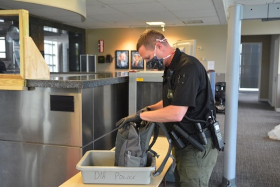 DIA Police Officer Scott Motes, wearing a protective face covering and gloves, inspects a bag while on-duty during the COVID-19 pandemic.