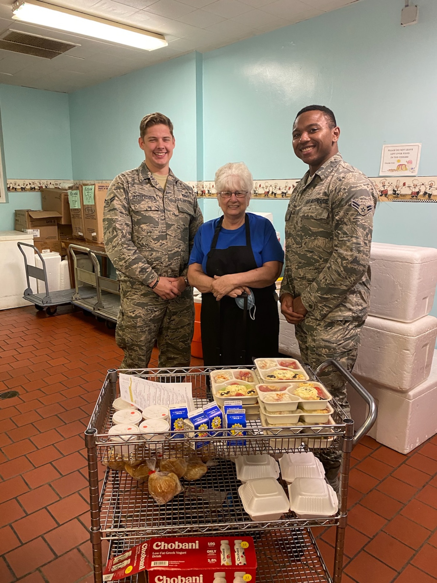 photo of two airmen and director of Okaloosa's Meals on Wheels pictured with food to be delivered to local seniors.