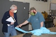 Logan Robinson, Letterkenny Army Depot (LEAD) (right), demonstrates an isolation gown prototype to James Eichelberger, WellSpan, at the LEAD upholstery shop on April 23, 2020. LEAD is currently producing personal protective equipment (PPE) for WellSpan to help combat COVID-19. (U.S. Army photo by Pam Goodhart)