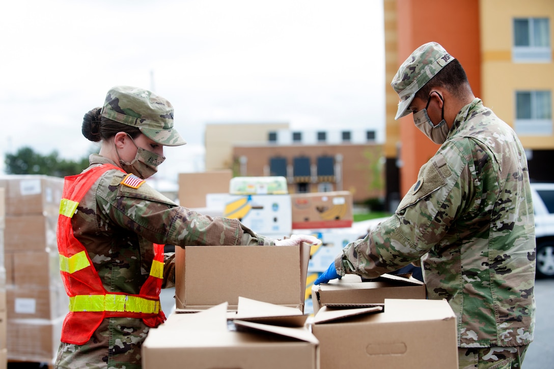 Two soldiers wearing masks prepare food boxes for a food distribution event.