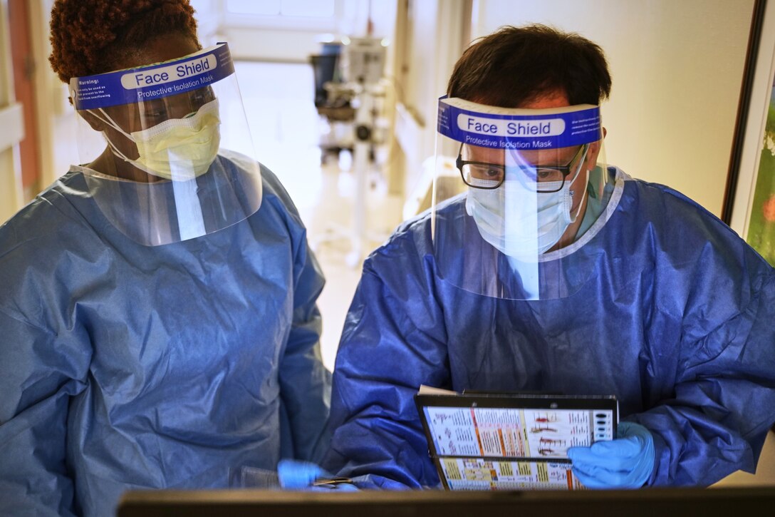 A pair of medical professionals wearing protective face masks and gowns review a patient’s chart.