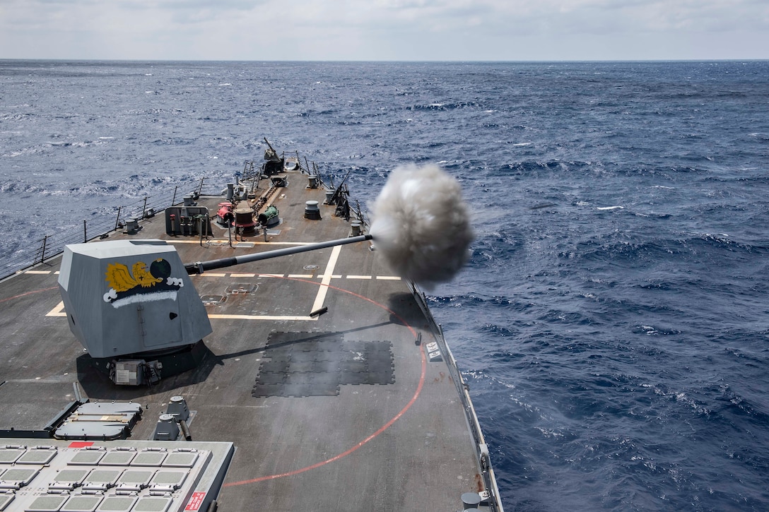 A military ship fires a large gun during a training exercise in the ocean.