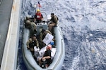 Military personnel in a boat alongside a ship.
