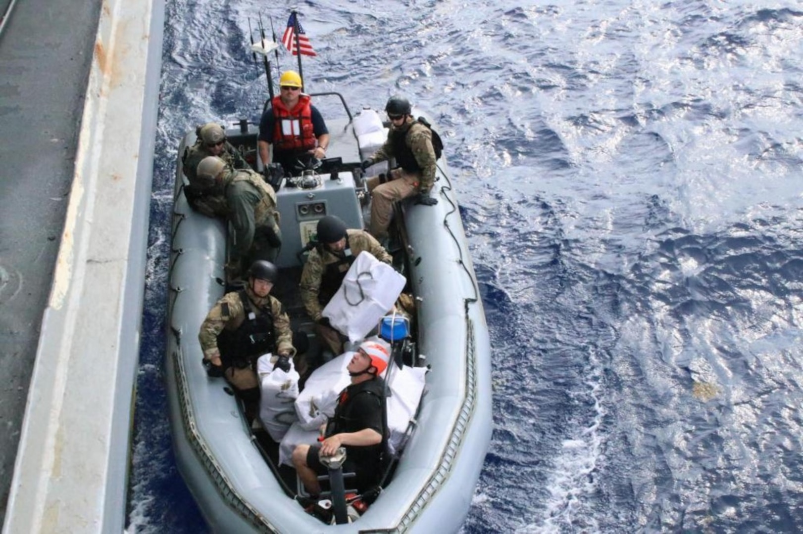 Military personnel in a boat alongside a ship.