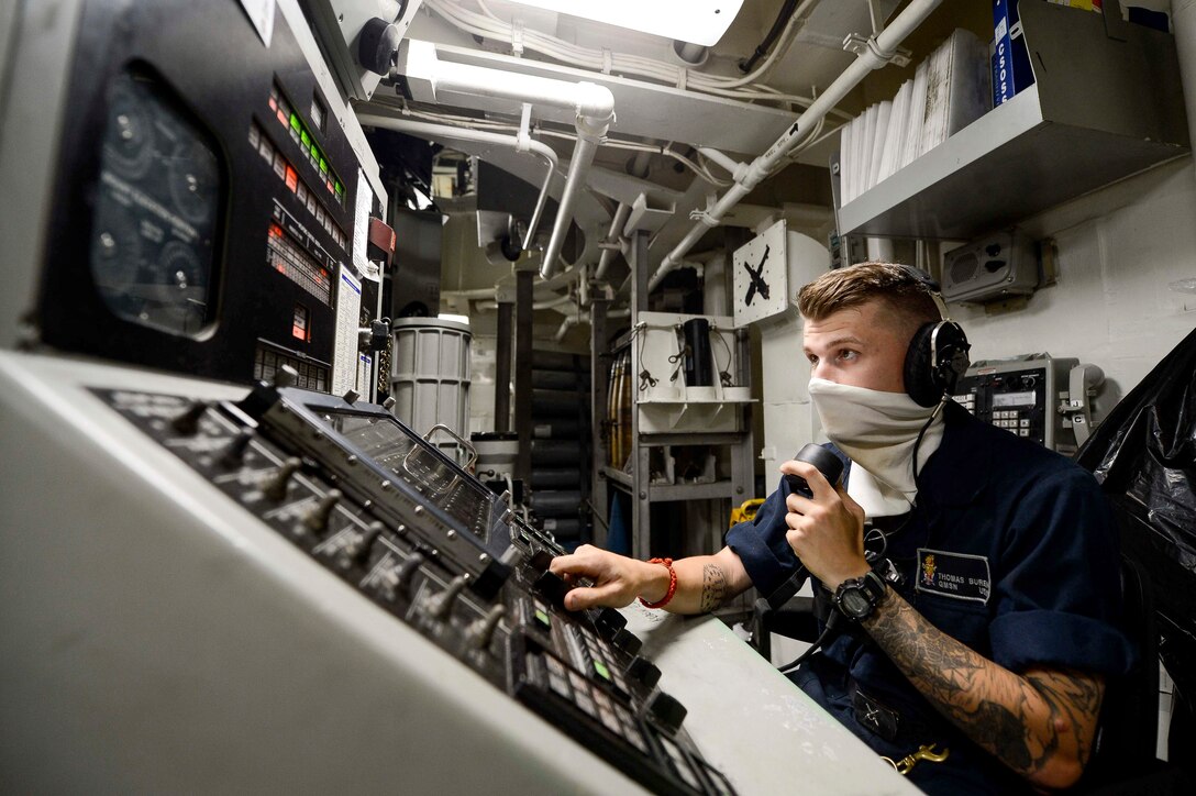 A sailor wearing a face mask works at a panel.