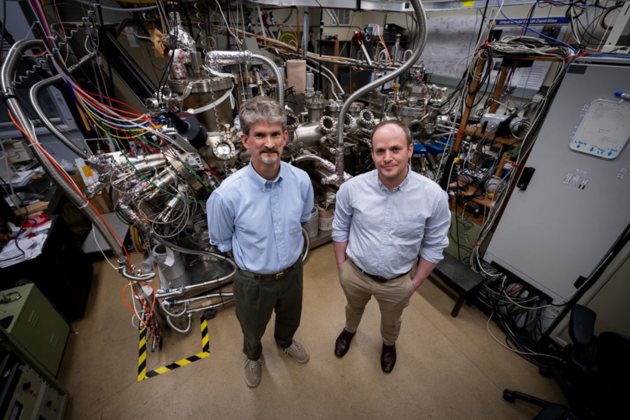 Two researchers pose in front a piece of research equipment.