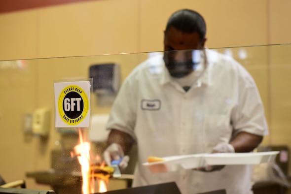 A social distancing reminder is displayed as Nelson O’Neal, Guardian Dining Facility (DFAC) cook, prepares a to-go meal for a customer at Creech Air Force Base, Nevada, April 17, 2020.