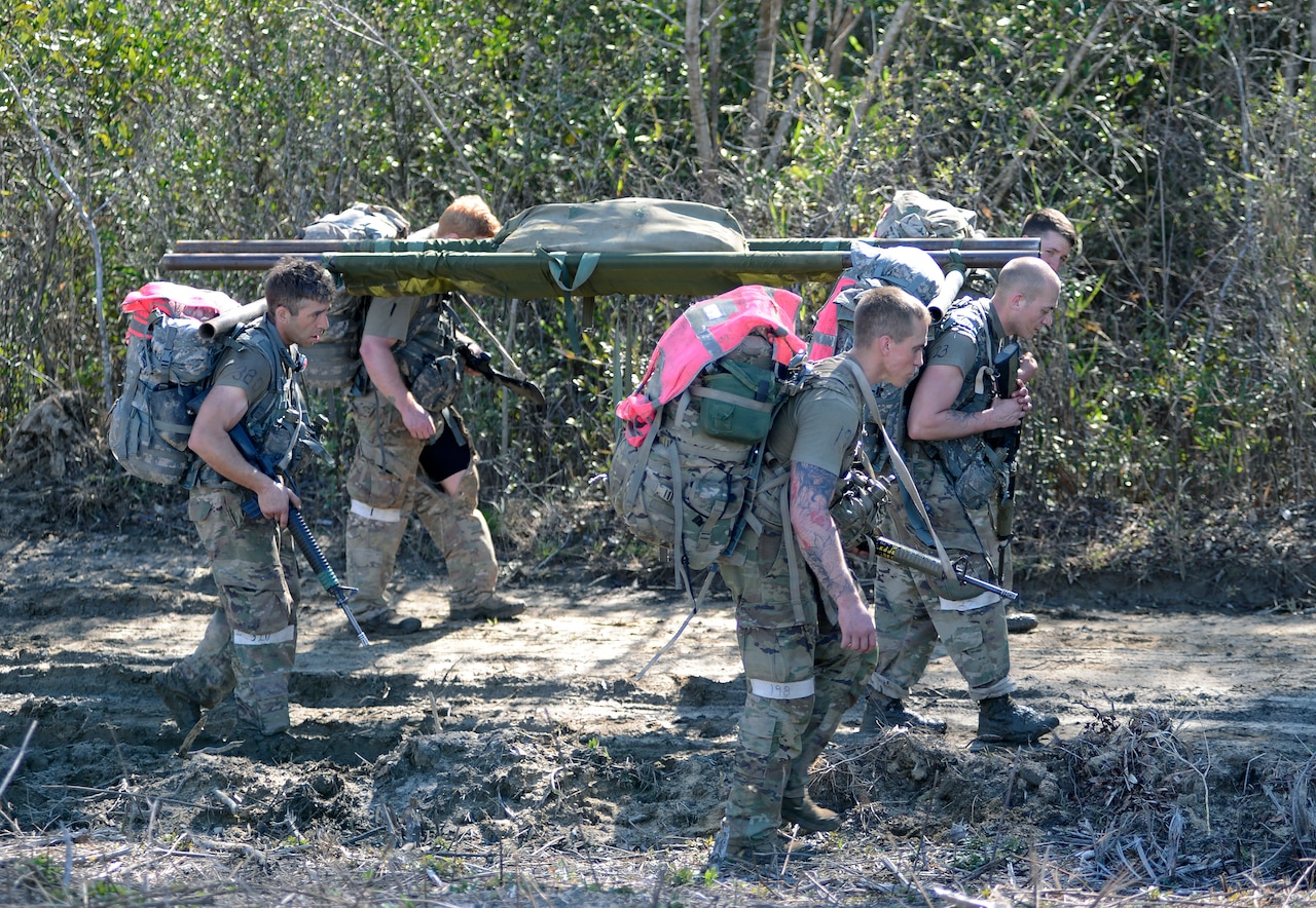 Soldiers carry a simulated patient on a litter over rugged terrain.