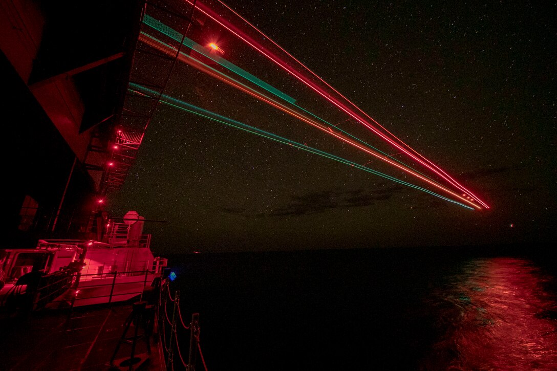 Beams of red lights shine on a ship at night.