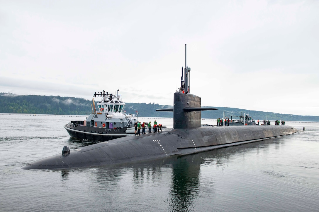 A group of people stand on top of a submarine next to a patrol boat.