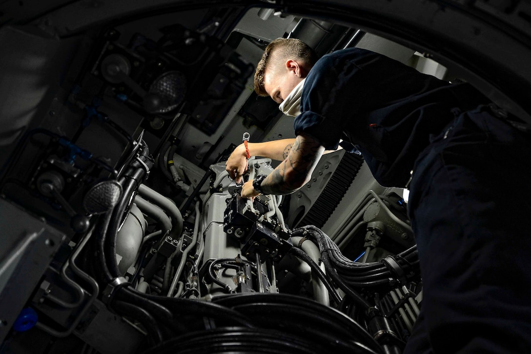 A sailor works on a large piece of machinery.