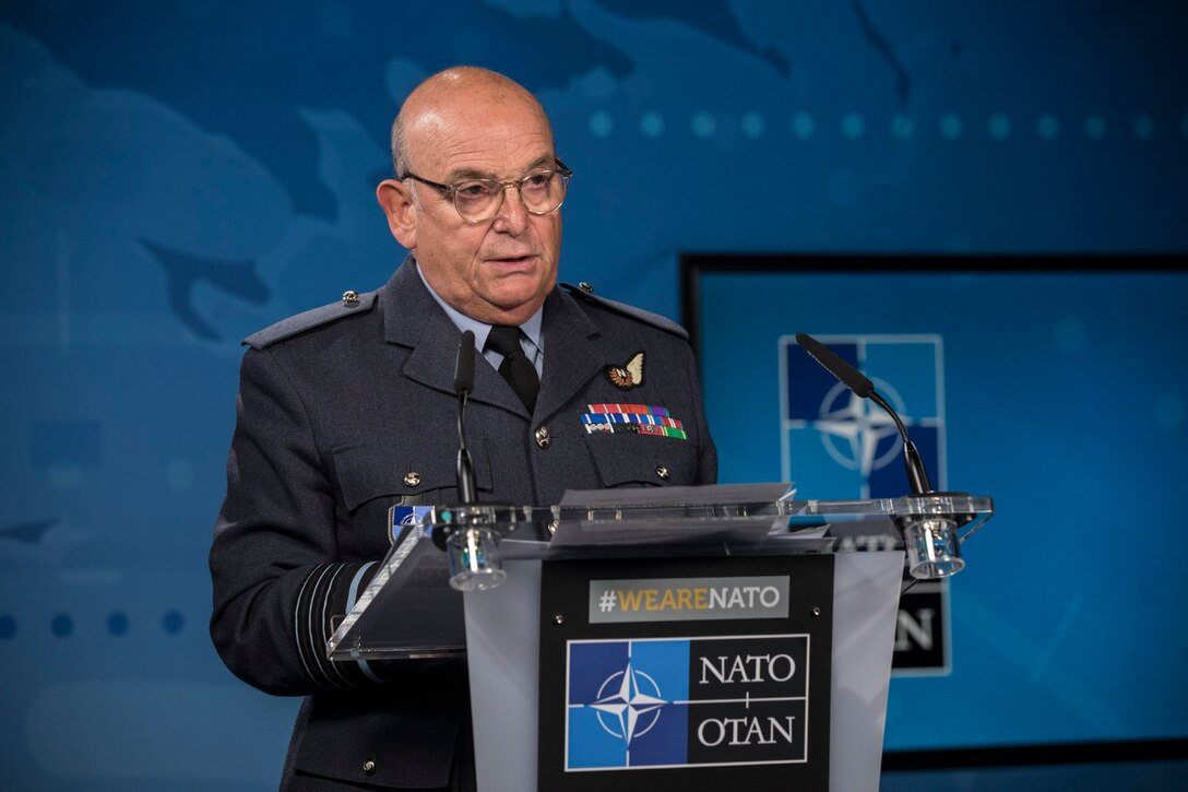 A man in a military uniform stands at a lectern.