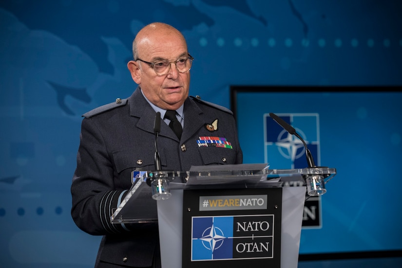 A man in a military uniform stands at a lectern.