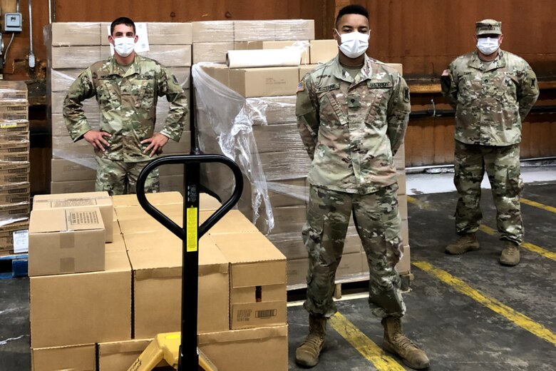 Photo of soldiers standing near pallets of food in a warehouse.