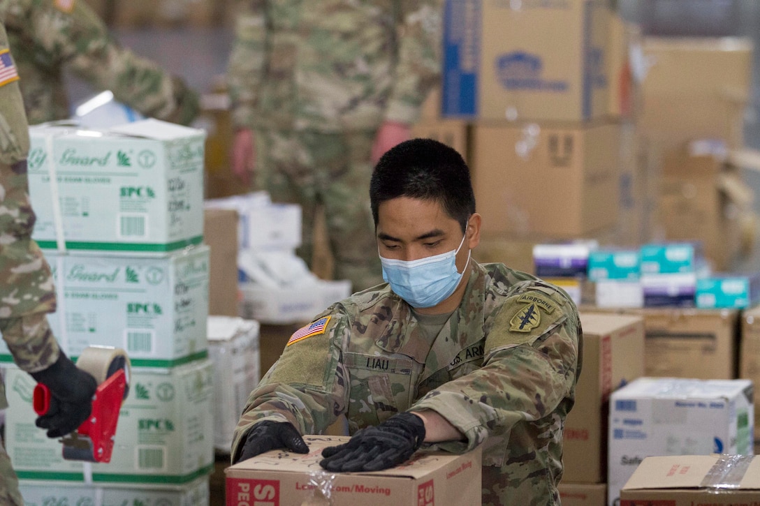 A National Guardsman wearing protective gear holds a box.