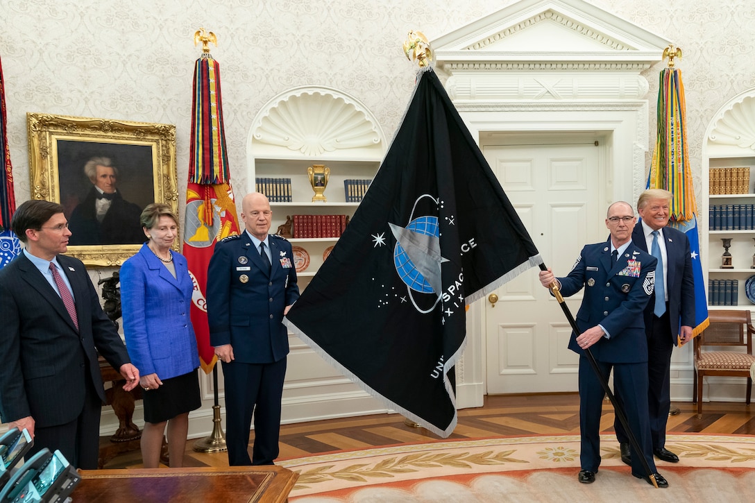 Men in military uniform hold a large flag while posing for a photo with three civilians.