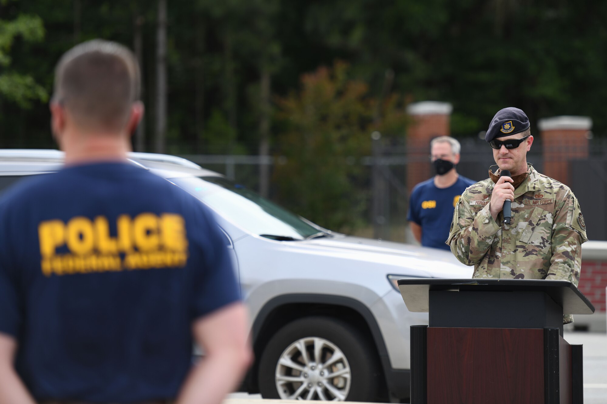 Man standing in formation with commander speaking in microphone