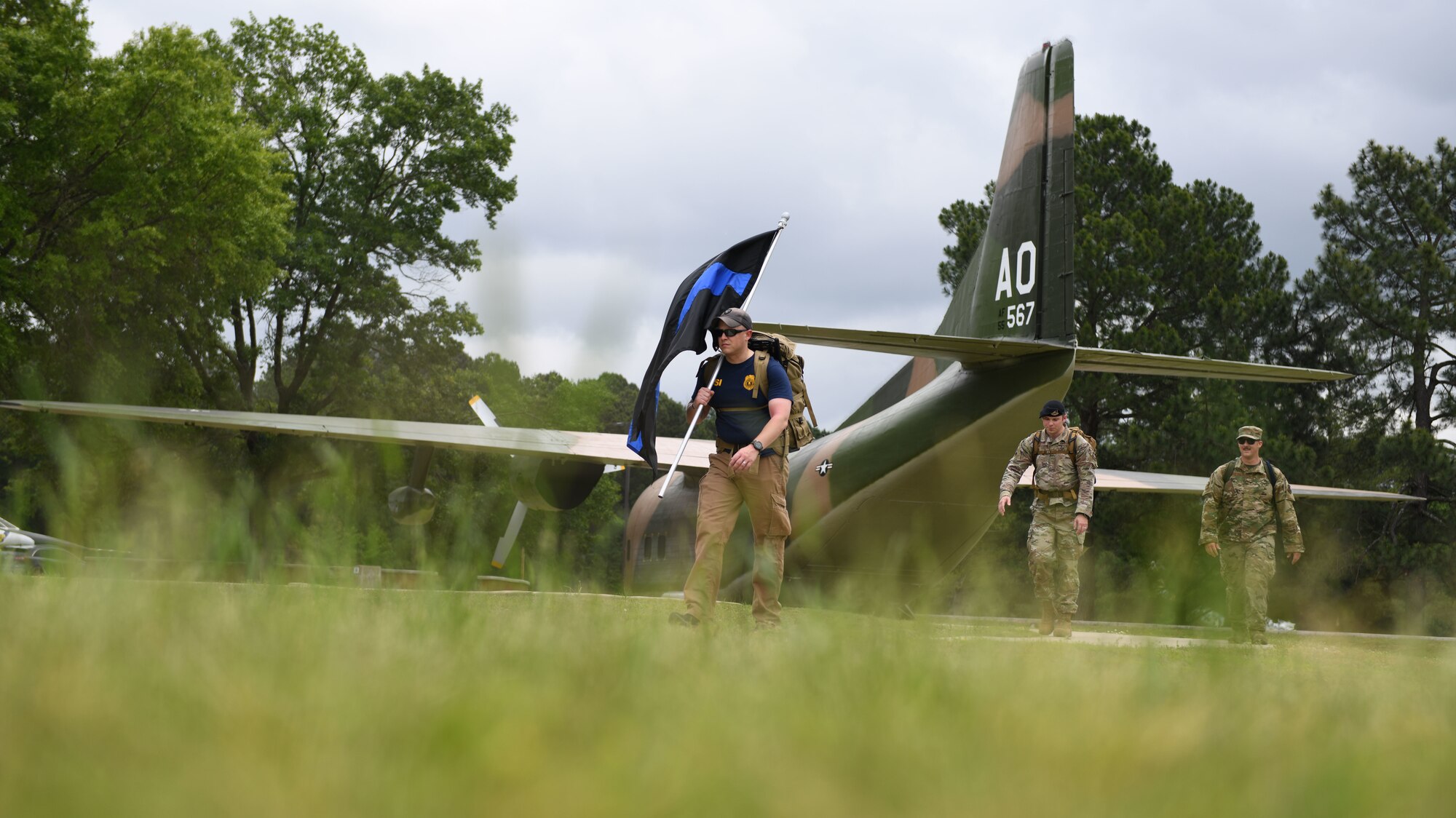 Man walking with Black flag with blue stripe down middle in front of a military Aircraft.