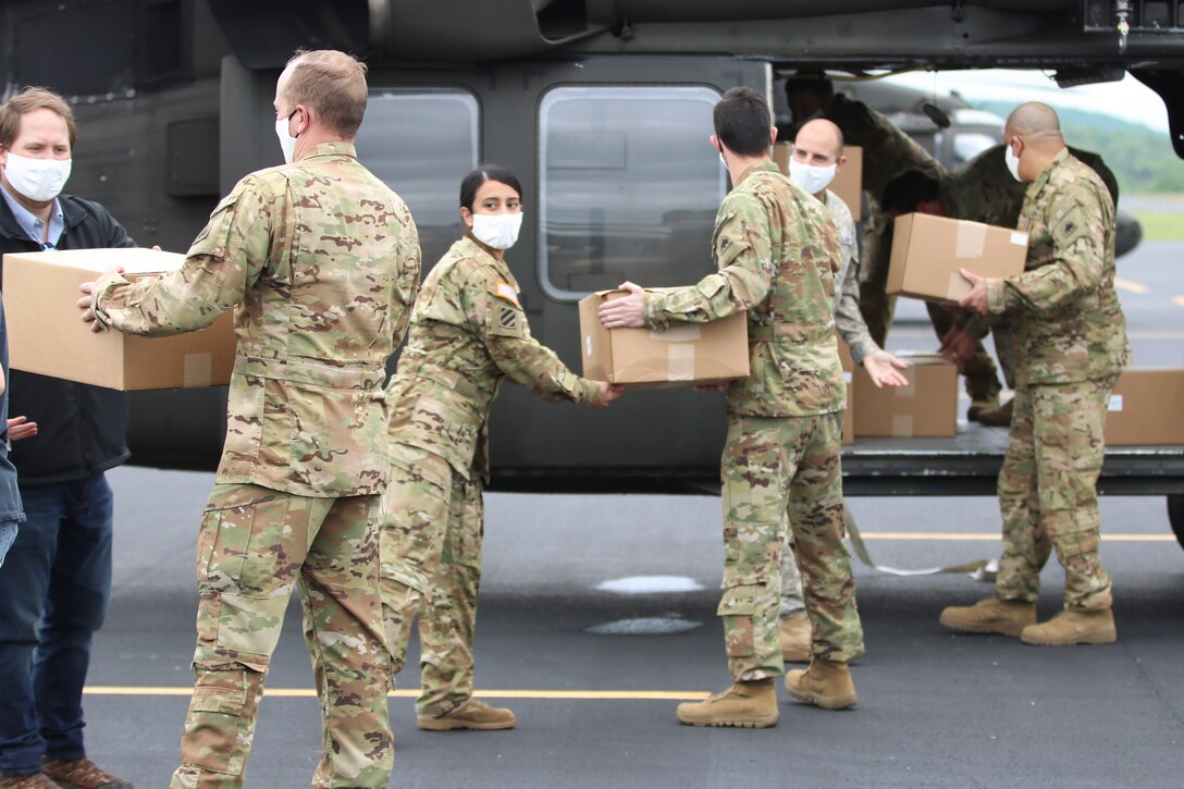 Soldiers in protective gear pass boxes to one another and then them on a helicopter.