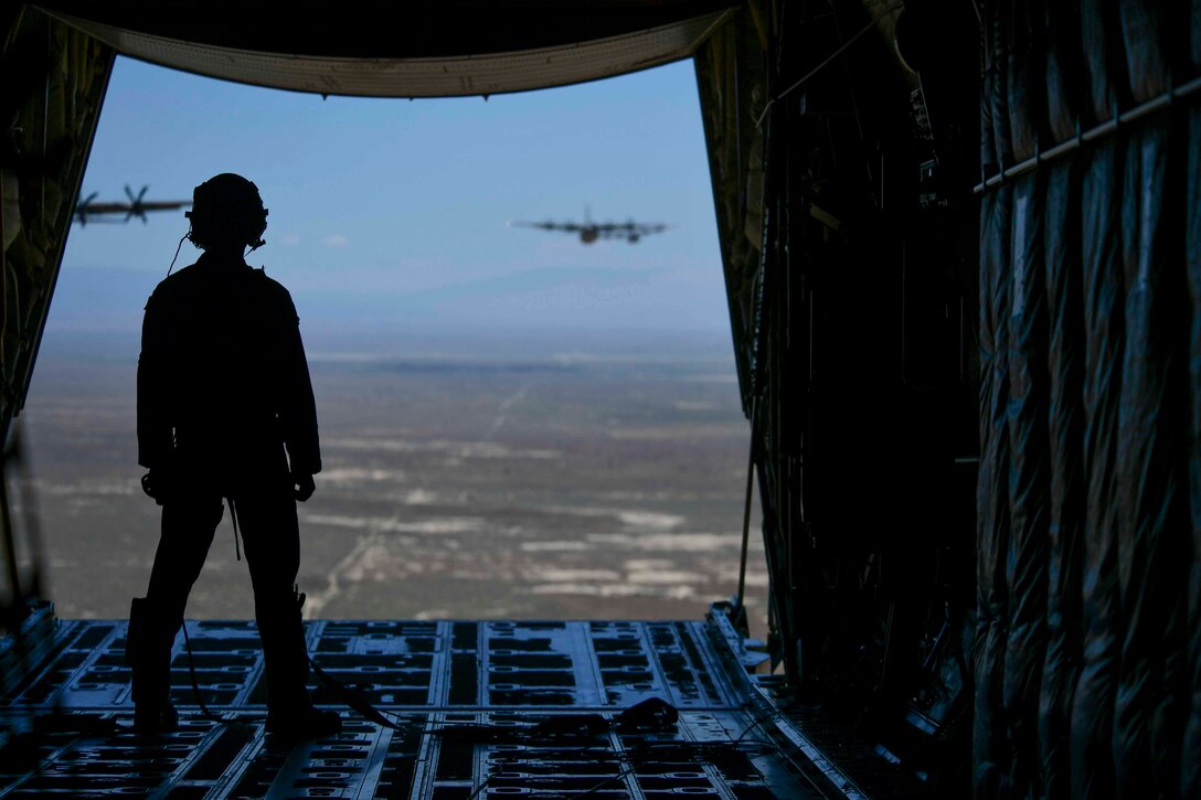 An airman stands at the back of an aircraft watching other aircraft fly in formation.