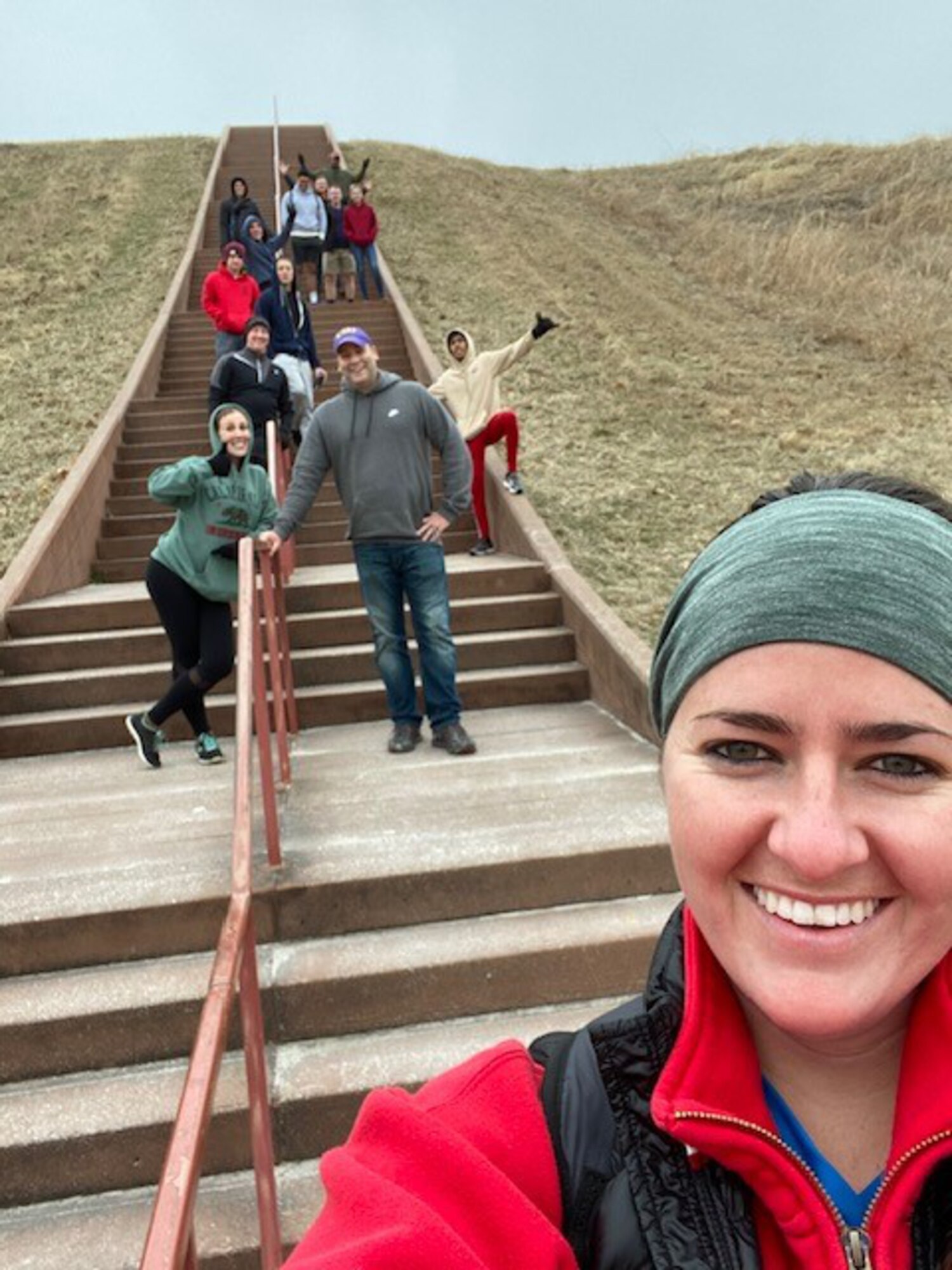 Woman taking selfie with people posing on stairs in background.