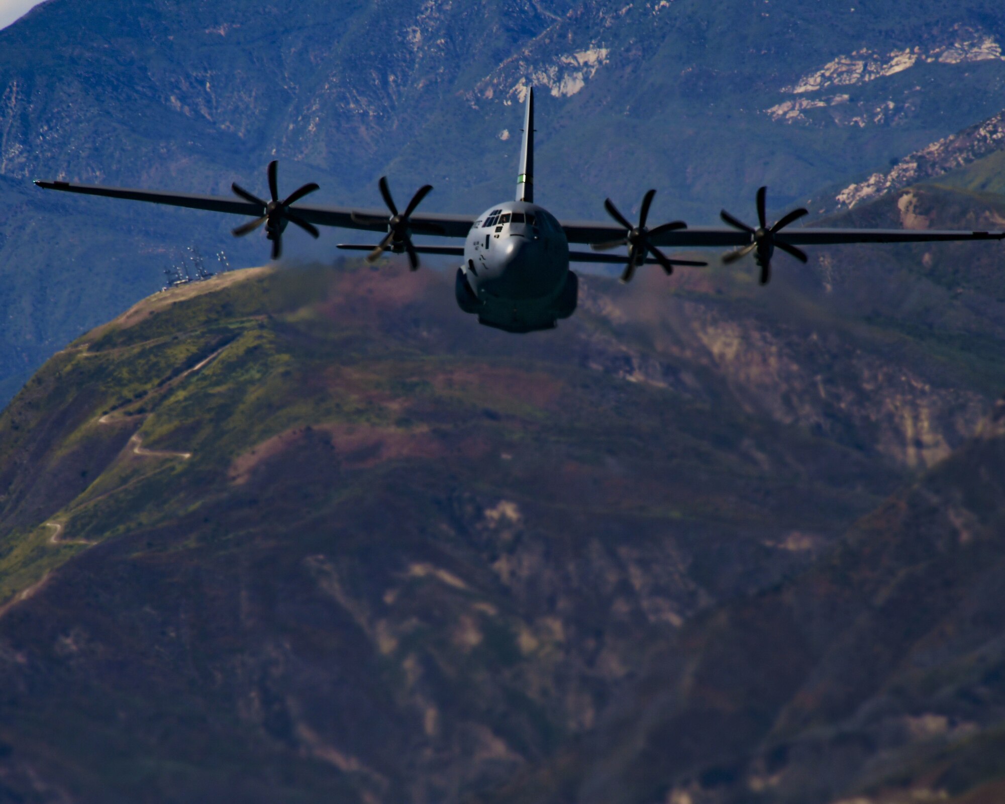 A military C-130J aircraft from the California Air National Guard fly's over green rolling hills above the city of Santa Barbara, California.