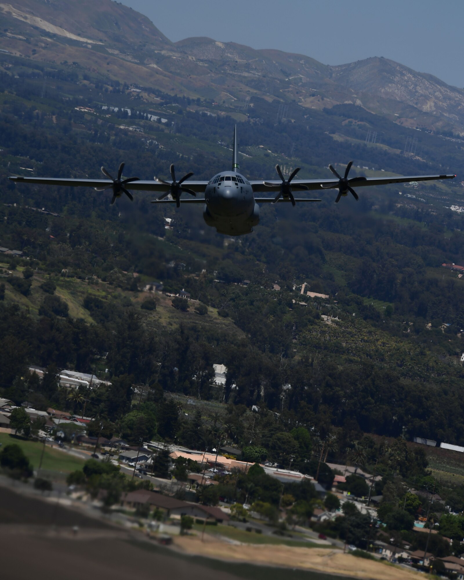 A military California Air National Guard C-130J Super Hercules aircraft is shown flying at a low altitude over the Camarillo Valley.