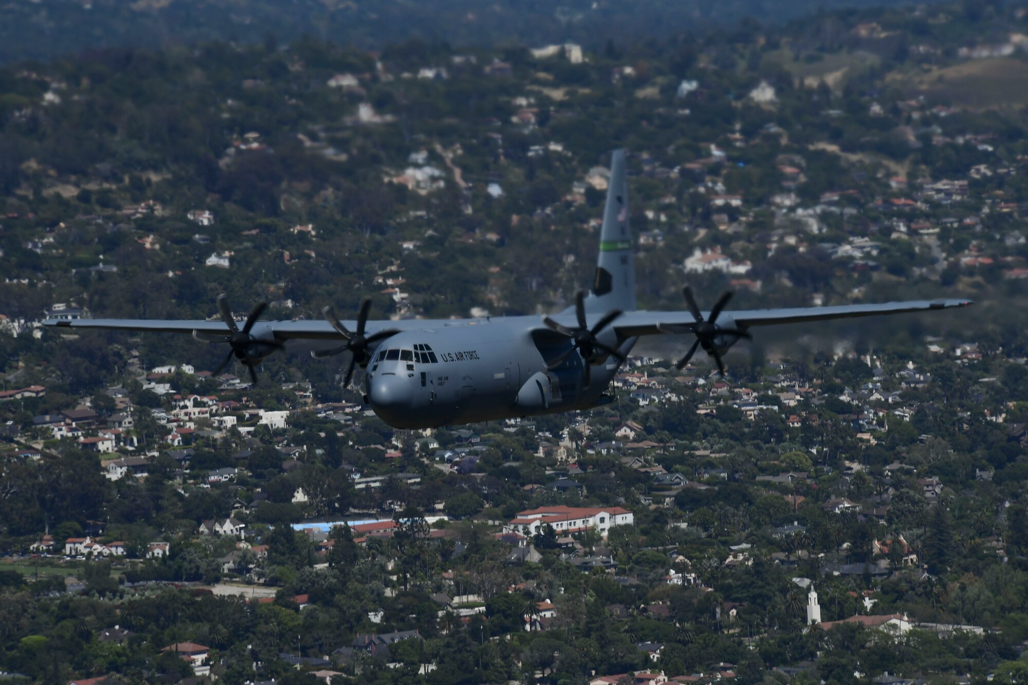 An image of a California Air National Guard C-130J Super Hercules aircraft flying over the Santa Barbara City skyline, California.