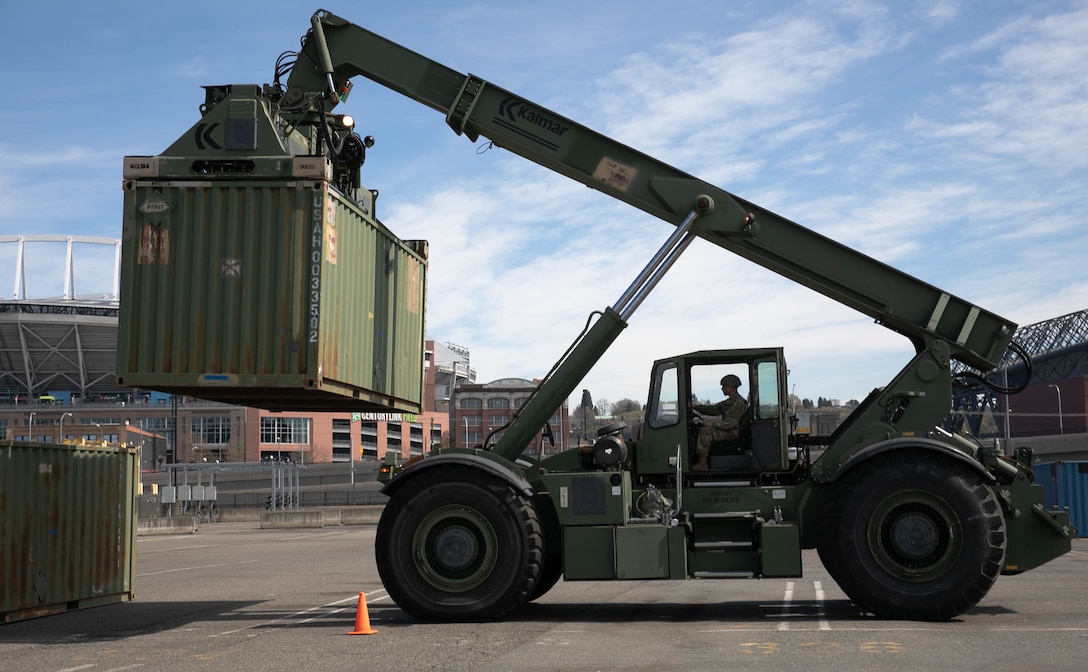 A soldier operates a vehicle as it moves a large container.