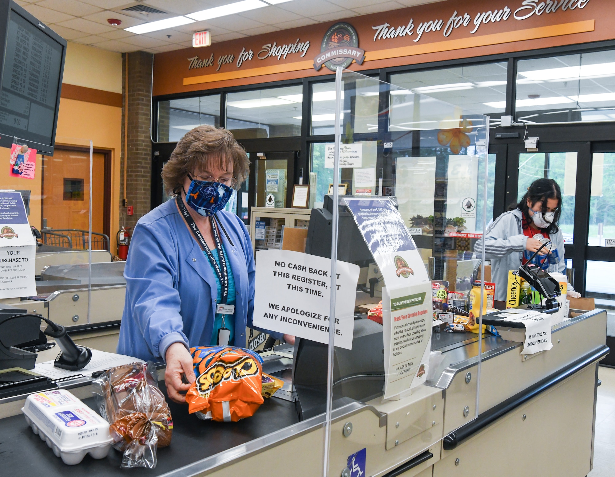 Store teller Tina Lawson scans a customer’s purchases, as bagger Sarah Goldston bags the items, May 5, 2020, at the Arnold Air Force Base Commissary, while taking measures to reduce the risk of coronavirus transmission. The Arnold Air Force Base Commissary and Base Exchange have remained open to serve their customers throughout the coronavirus crisis. (U.S. Air Force photo by Jill Pickett) (This image was altered by obscuring a badge for security purposes.)