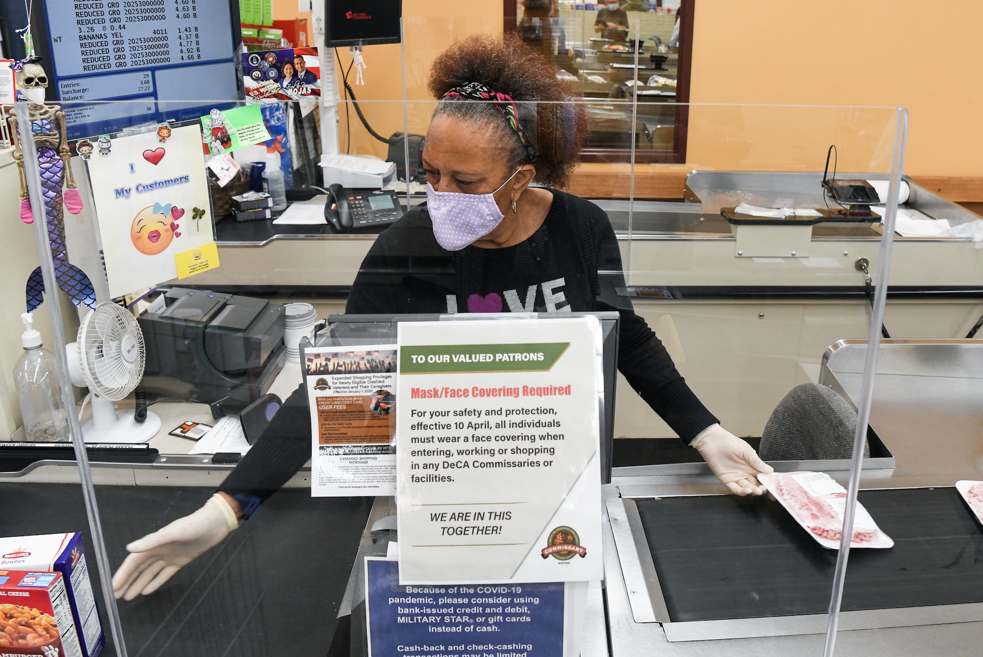 Store teller Wynetta Johnson scans a customer's purchases May 5, 2020, at the Arnold Air Force Base Commissary, while taking measures to reduce the risk of coronavirus transmission. The Arnold Air Force Base Commissary and Base Exchange have remained open to serve their customers throughout the coronavirus crisis. (U.S. Air Force photo by Jill Pickett)