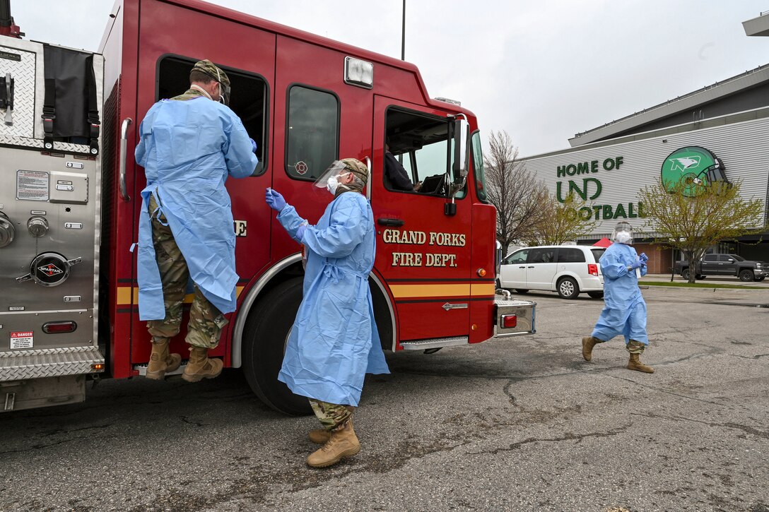 National Guardsmen in protective gear stand at a firetruck in a parking lot.