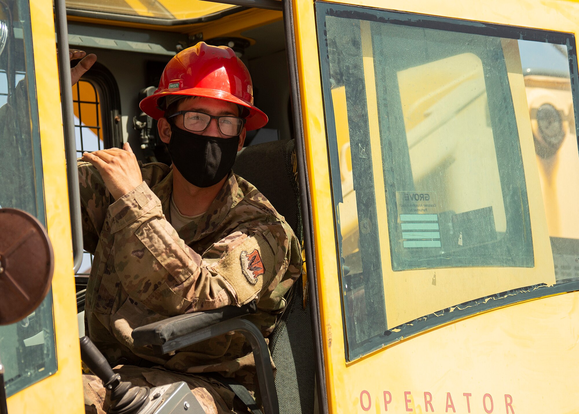 A RED HORSE Airman uses his hands to signal another Airman while operating a 30-ton crane.