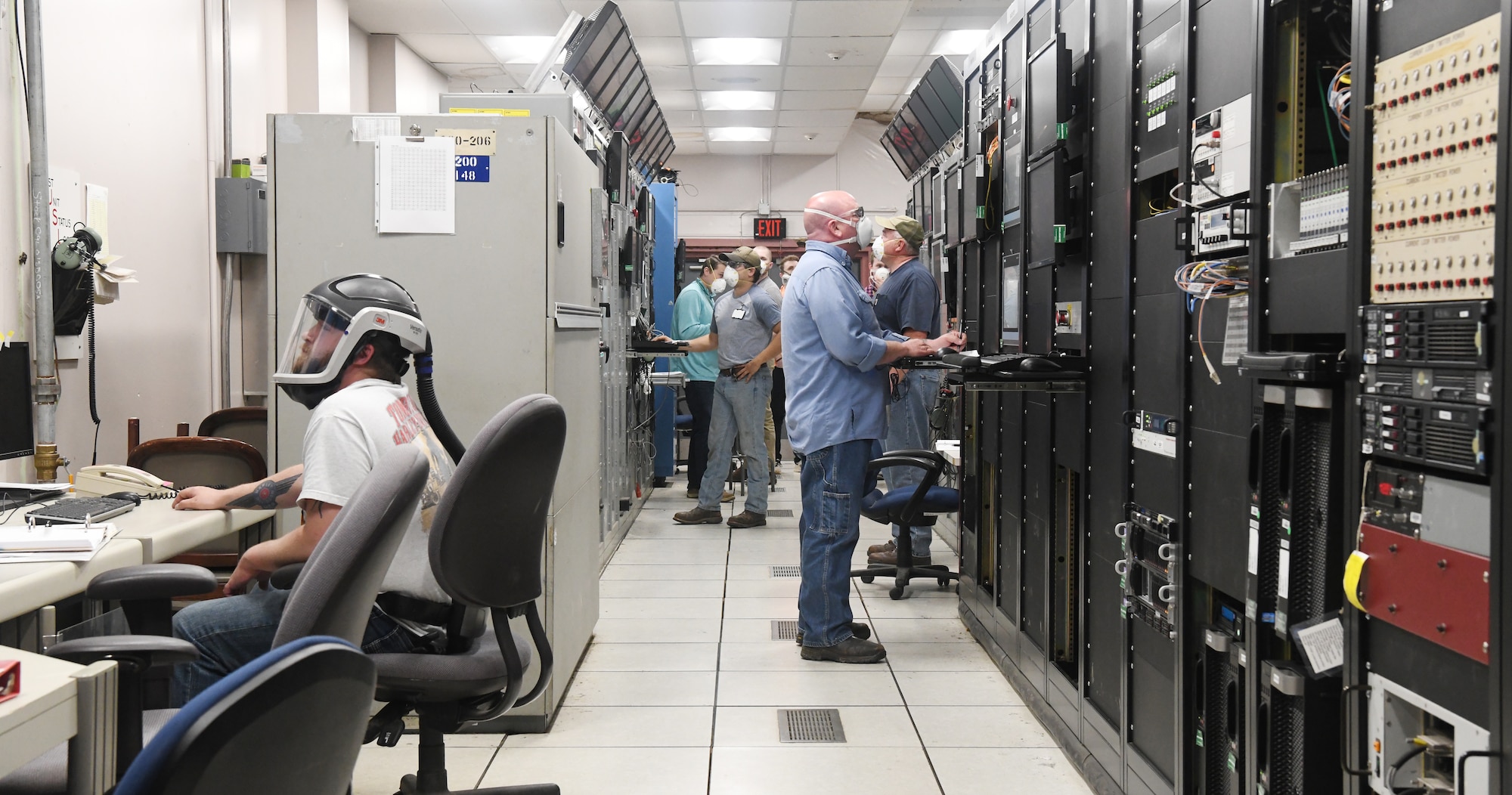 Seven Hroncich, left, an instrument technician, Robert Bradford, center right, an electrician, Kevin Thompson, right, test operations engineer, Tim Mullins, an outside machinist, and others prepare for a test run in the Arnold Engineering Development Complex (AEDC) Arcs Test Facility Control Room, May 5, 2020, at Arnold Air Force Base, Tenn. The Arcs Facility provides aerothermal ground test simulations of hypersonic flight over a wide range of velocities and pressure altitudes in support of materials and structures development. Team members are maintaining social distancing when possible and wearing masks when not so they can continue the critical national defense mission of AEDC. (U.S. Air Force photo by Jill Pickett) (This image was altered by obscuring items for security purposes.)