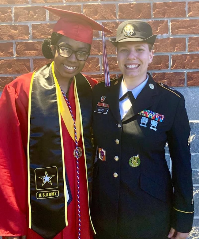 Future Soldier dressed in graduation cap and gown poses with female Soldier, Sgt. Mort, who is wear her Army dress uniform.