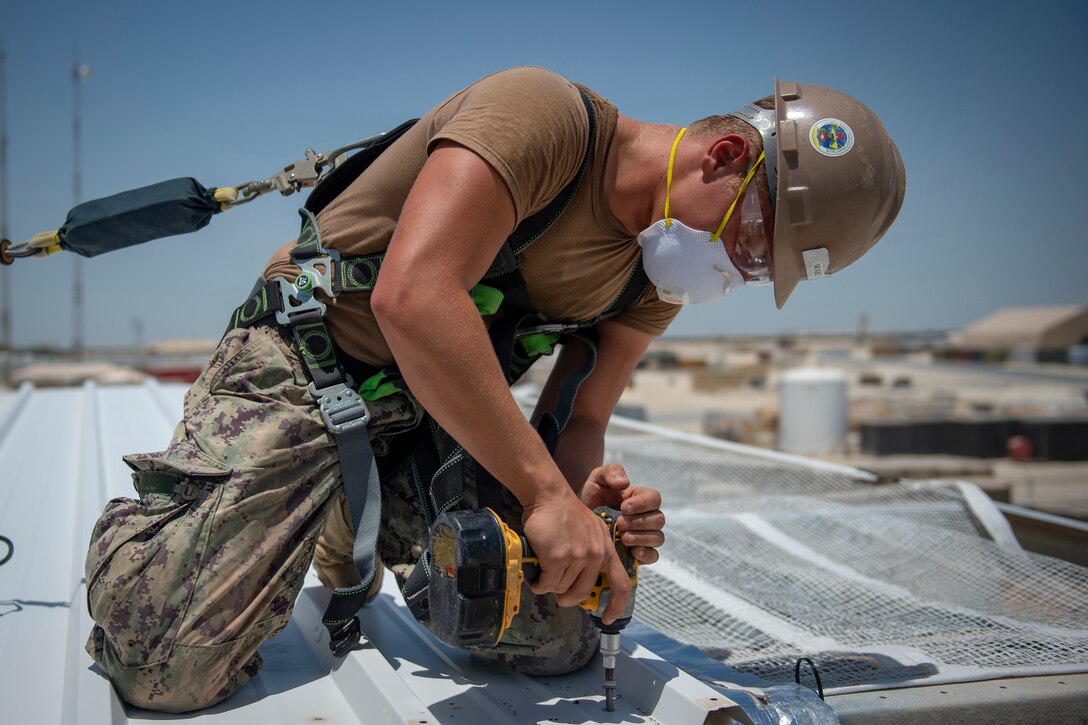 A Seabee drills a nail into a roof.