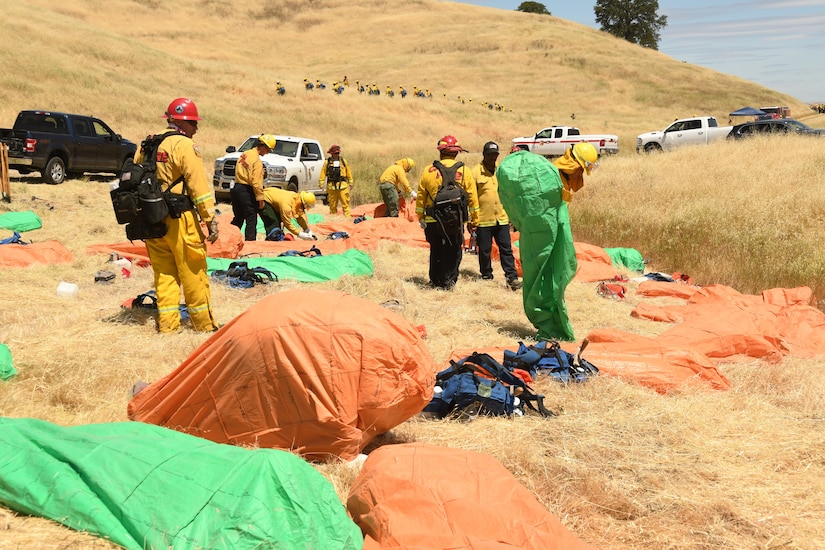 Soldiers wearing fire-protection equipment prepare to erect small tents.